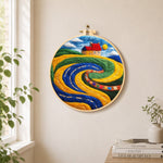 Abstract swirling fields and red roof cottage needle felt wall art displayed in a bright home interior