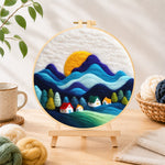 Finished abstract wavy mountains and tiny houses needle felting displayed on a wooden easel