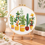 Assorted houseplants embroidery kit finished hoop displayed on a wooden stand as cozy tabletop decor