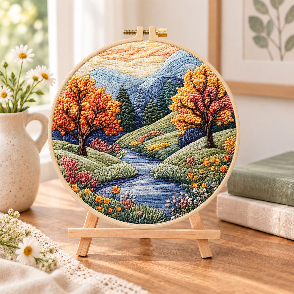 Autumn creek and trees embroidery kit finished hoop displayed on a wooden stand as cozy tabletop decor