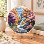Autumn forest stream embroidery kit finished hoop displayed on a wooden stand as cozy tabletop decor