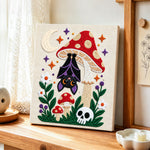 Bat hanging under mushroom punch needle artwork displayed on a table