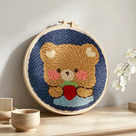 Bear holding strawberry punch needle artwork displayed on a table