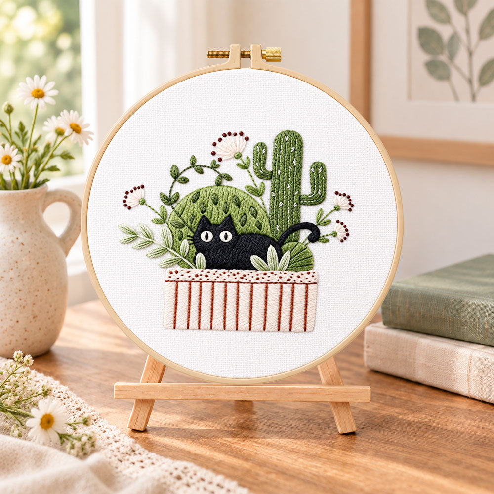 Black cat and cactus embroidery kit finished hoop displayed on a wooden stand as cozy tabletop decor