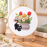Black cat and tulips embroidery kit finished hoop displayed on a wooden stand as cozy tabletop decor