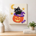 Finished black cat inside pumpkin hat artwork displayed on a wall