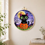 Black cat with green eyes on pumpkin needle felt wall art displayed in a bright home interior