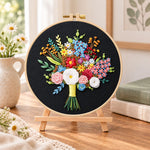 Black fabric flower bouquet embroidery kit finished hoop displayed on a wooden stand as cozy tabletop decor