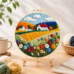 Finished blooming flower field and red roof cottage needle felting displayed on a wooden easel