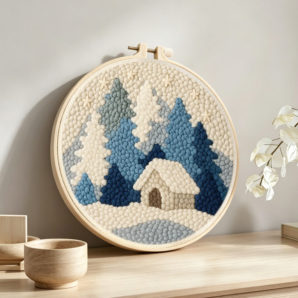 Blue and white snowy cabin in the woods punch needle artwork displayed on a table