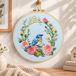 Blue bird inside pink rose wreath embroidery hoop wall art displayed as warm and cozy handmade home decor
