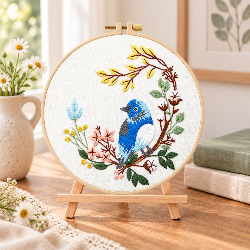Blue bird on floral branch embroidery kit finished hoop displayed on a wooden stand as cozy tabletop decor