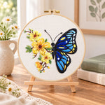 Blue butterfly with yellow blooms embroidery kit finished hoop displayed on a wooden stand as cozy tabletop decor