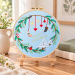 Blue christmas wreath embroidery kit finished hoop displayed on a wooden stand as cozy tabletop decor