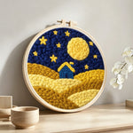 Blue house on yellow hills under the starry sky punch needle artwork displayed on a table