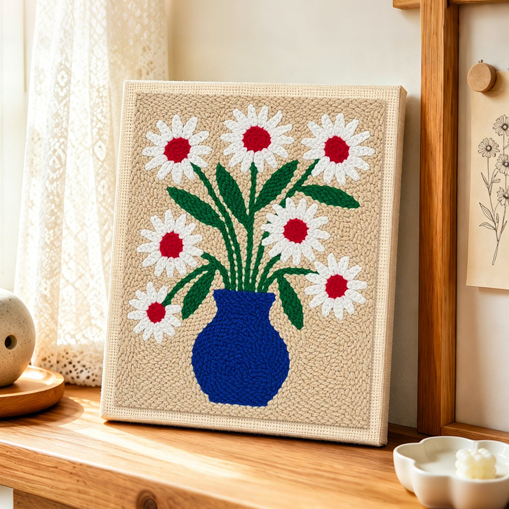 Blue vase with red-centred daisies punch needle artwork displayed on a table