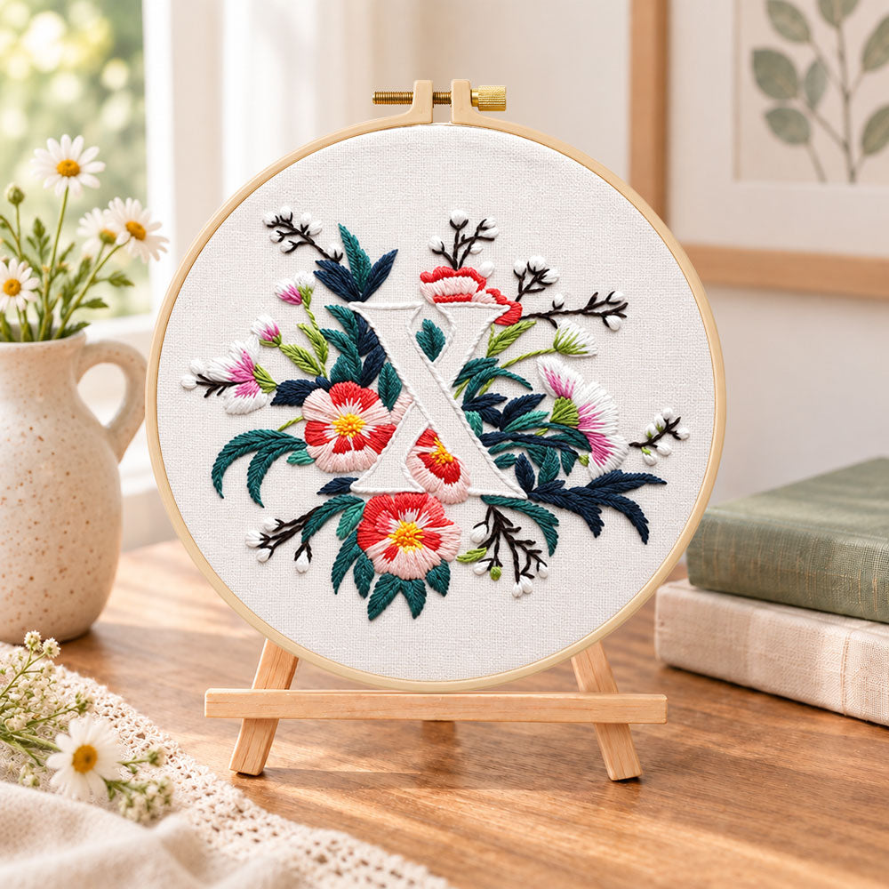 Blush florals and letter x embroidery kit finished hoop displayed on a wooden stand as cozy tabletop decor
