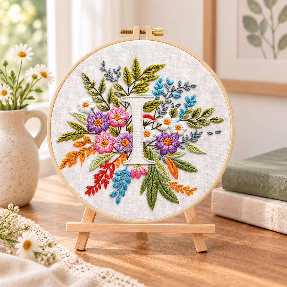 Bright mixed petals and letter i embroidery kit finished hoop displayed on a wooden stand as cozy tabletop decor