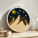Brown and white snowy mountains under a starry sky punch needle artwork displayed on a table