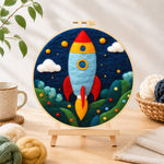 Finished cartoon rocket launch needle felting displayed on a wooden easel