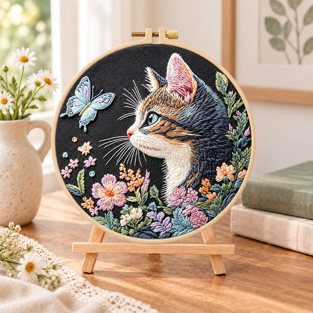 Cat and blue butterfly embroidery kit finished hoop displayed on a wooden stand as cozy tabletop decor