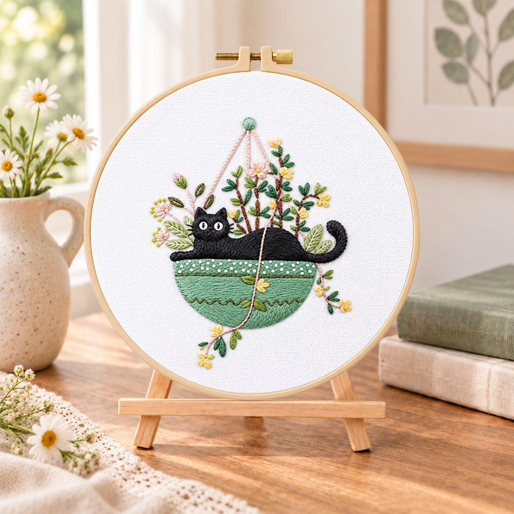 Cat in green hanging pot embroidery kit finished hoop displayed on a wooden stand as cozy tabletop decor