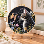 Cat watching butterfly embroidery kit finished hoop displayed on a wooden stand as cozy tabletop decor