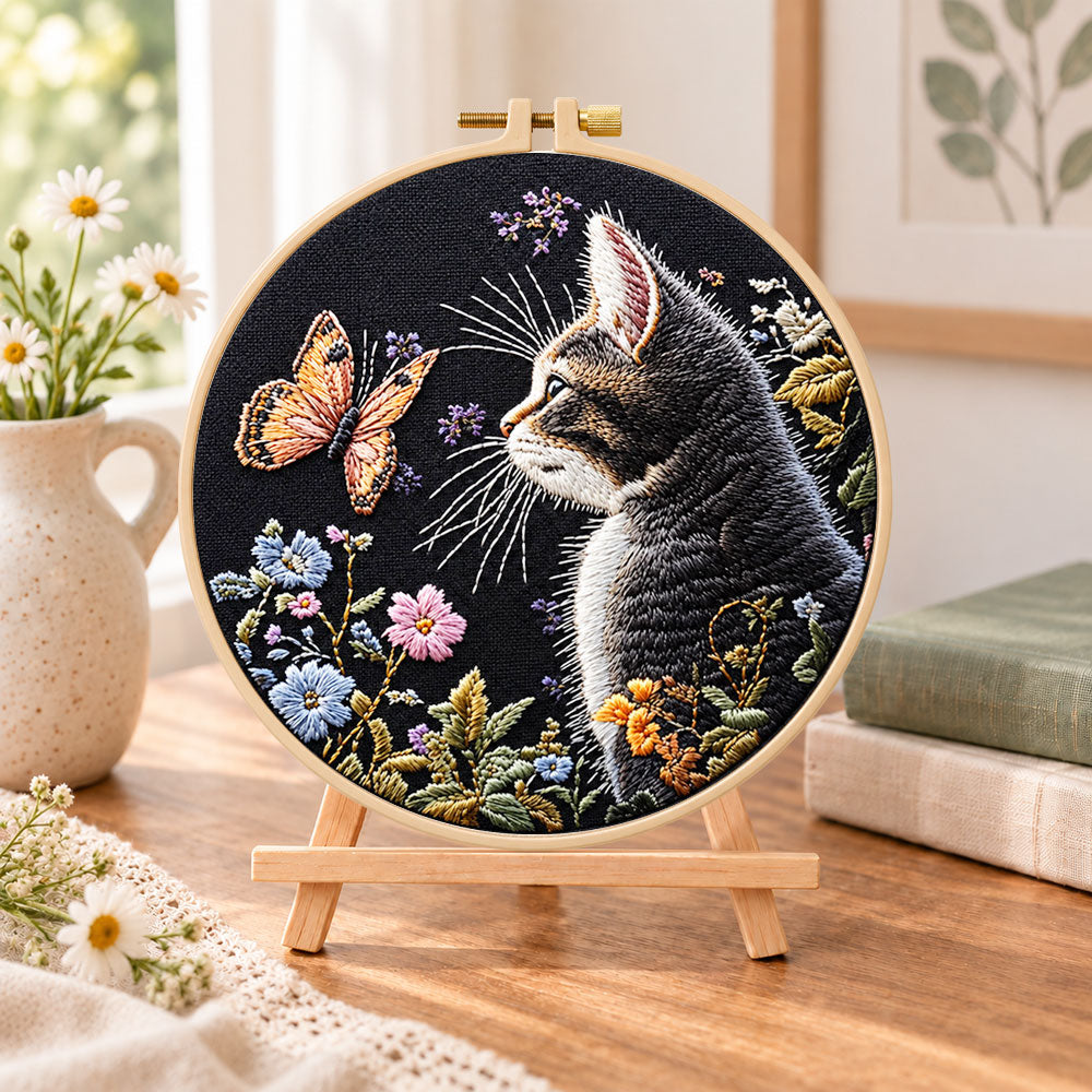 Cat watching butterfly embroidery kit finished hoop displayed on a wooden stand as cozy tabletop decor