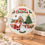 Christmas cabin and tree embroidery kit finished hoop displayed on a wooden stand as cozy tabletop decor