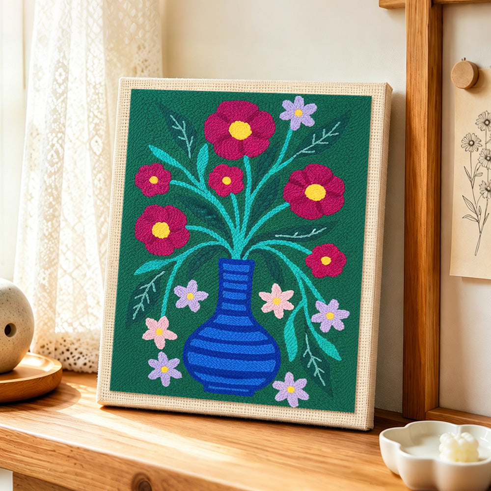 Colorful flowers in striped blue vase punch needle artwork displayed on a table