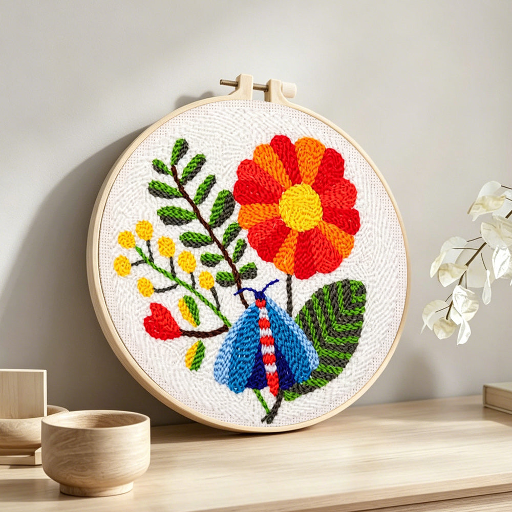 Colorful moth and large flower punch needle artwork displayed on a table