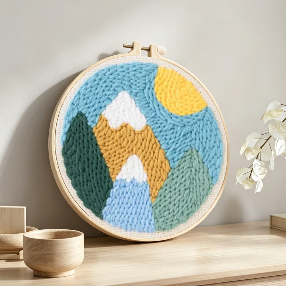 Colorful mountain landscape with sun punch needle artwork displayed on a table