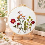 Cotton and burgundy flower arrangement embroidery kit finished hoop displayed on a wooden stand as cozy tabletop decor