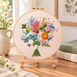 Cream wildflower bouquet embroidery kit finished hoop displayed on a wooden stand as cozy tabletop decor