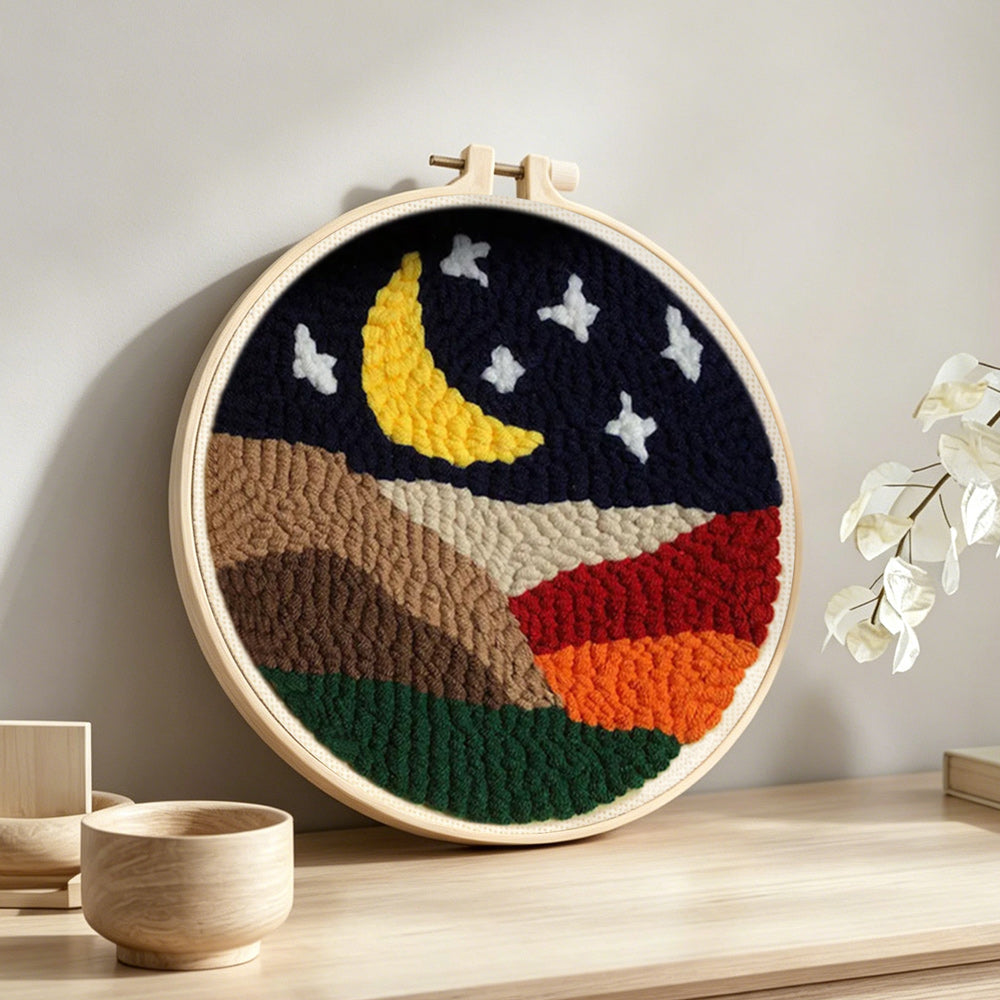 Crescent moon and white stars above the colorful mountains punch needle artwork displayed on a table