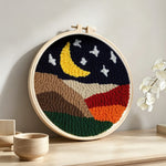 Crescent moon and white stars above the colorful mountains punch needle artwork displayed on a table