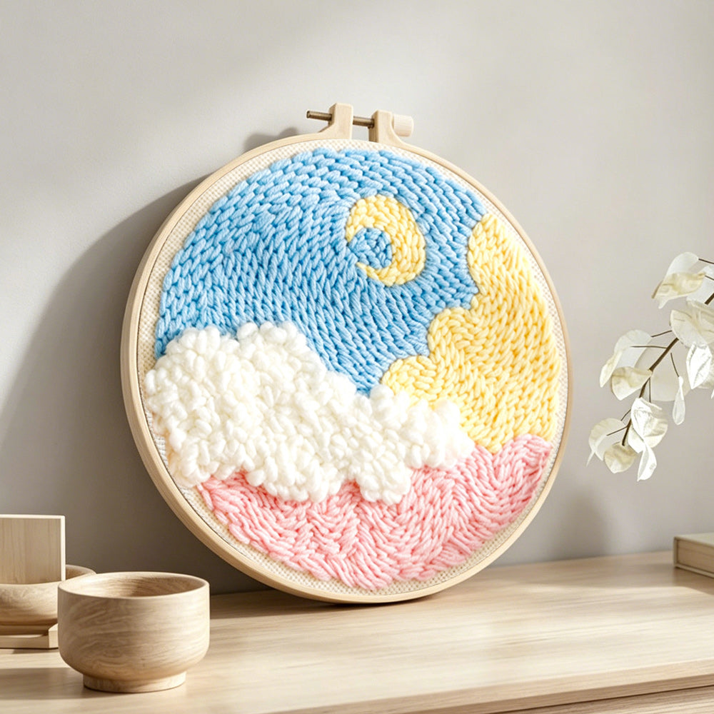 Crescent moon over colorful clouds punch needle artwork displayed on a table