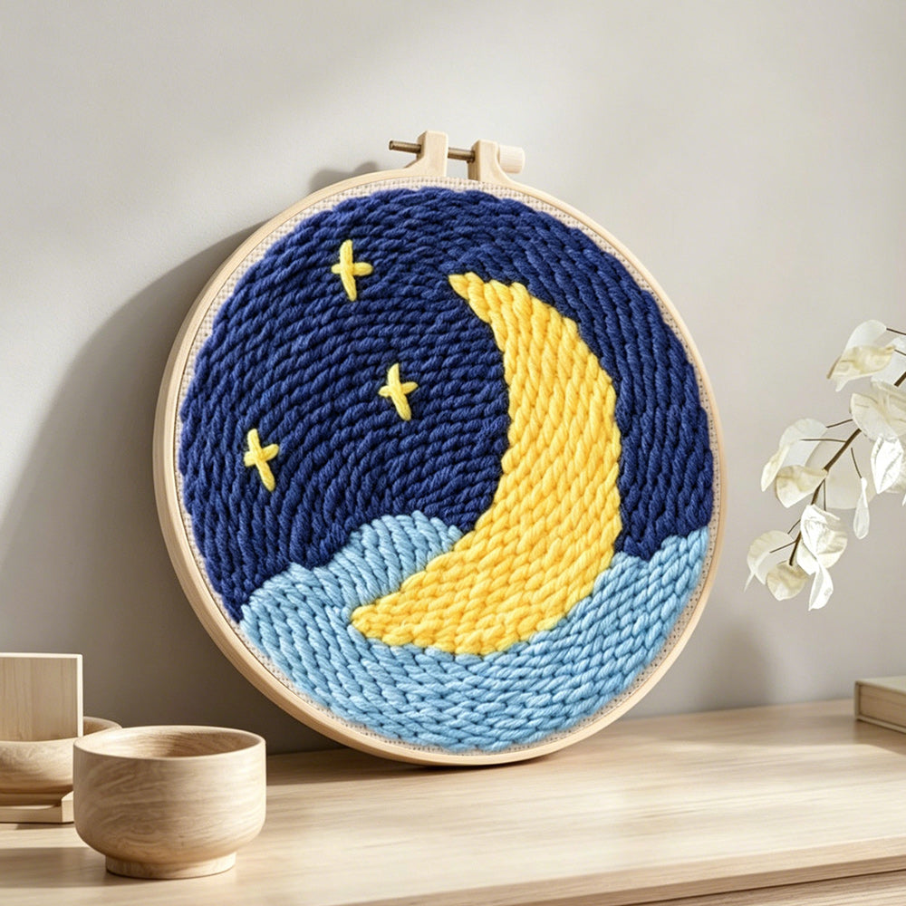 Crescent moon over starry night sky punch needle artwork displayed on a table