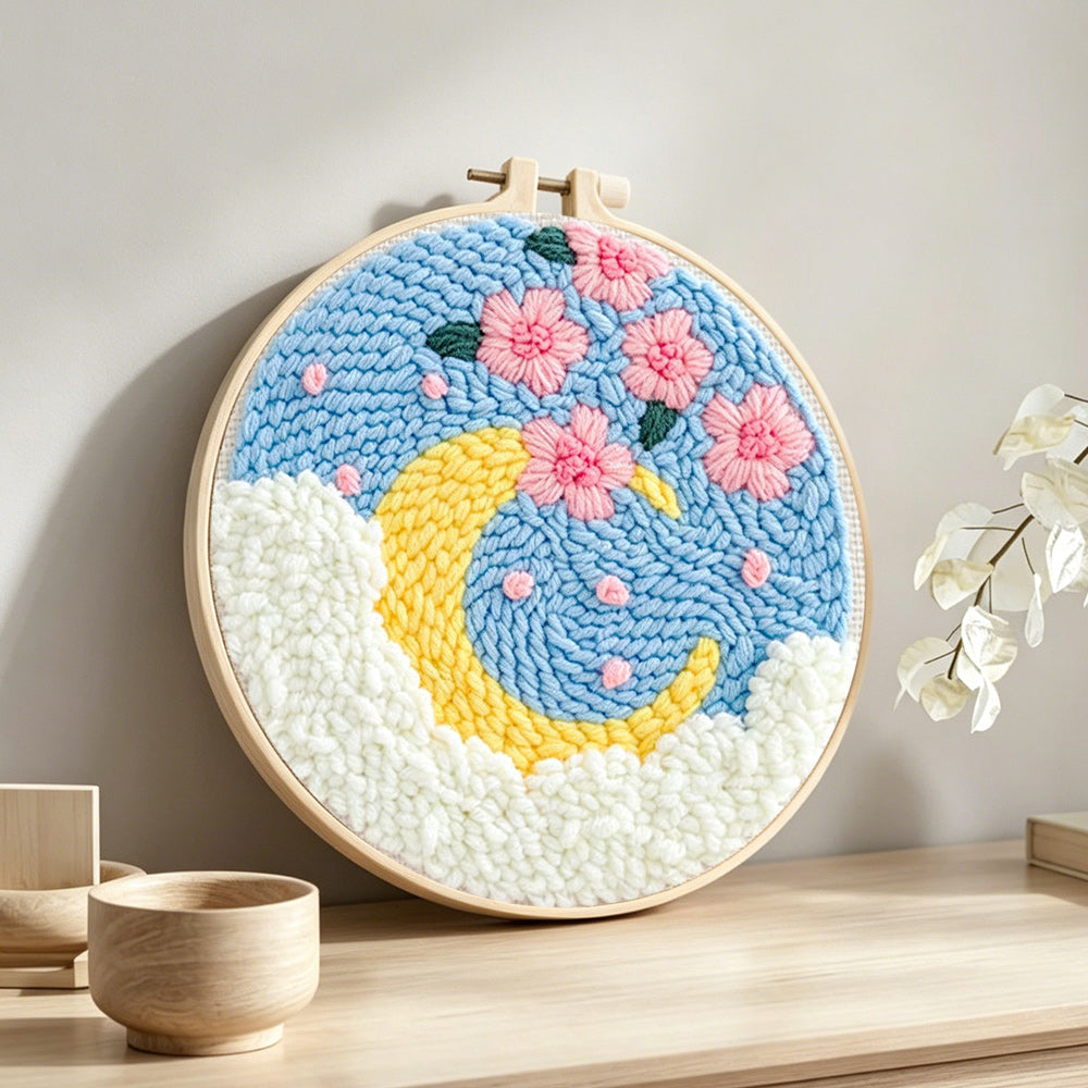 Crescent moon with pink flowers punch needle artwork displayed on a table