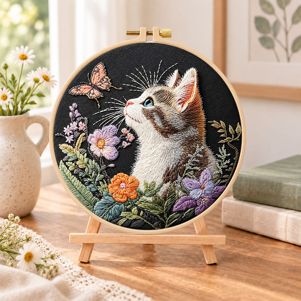 Curious cat and pink butterfly embroidery kit finished hoop displayed on a wooden stand as cozy tabletop decor