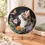Curious cat and pink butterfly embroidery kit finished hoop displayed on a wooden stand as cozy tabletop decor