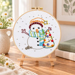 Cute snowman and tree embroidery kit finished hoop displayed on a wooden stand as cozy tabletop decor