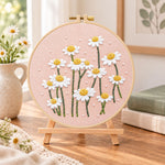 Daisies on dusty pink fabric embroidery kit finished hoop displayed on a wooden stand as cozy tabletop decor