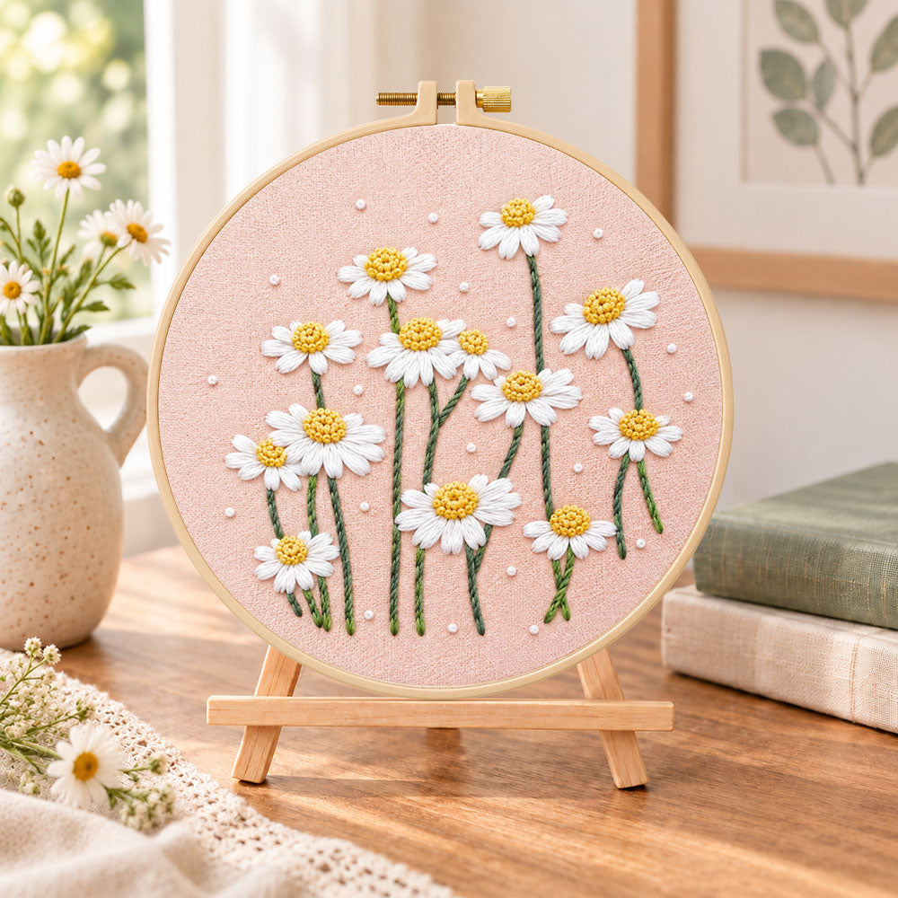 Daisies on dusty pink fabric embroidery kit finished hoop displayed on a wooden stand as cozy tabletop decor