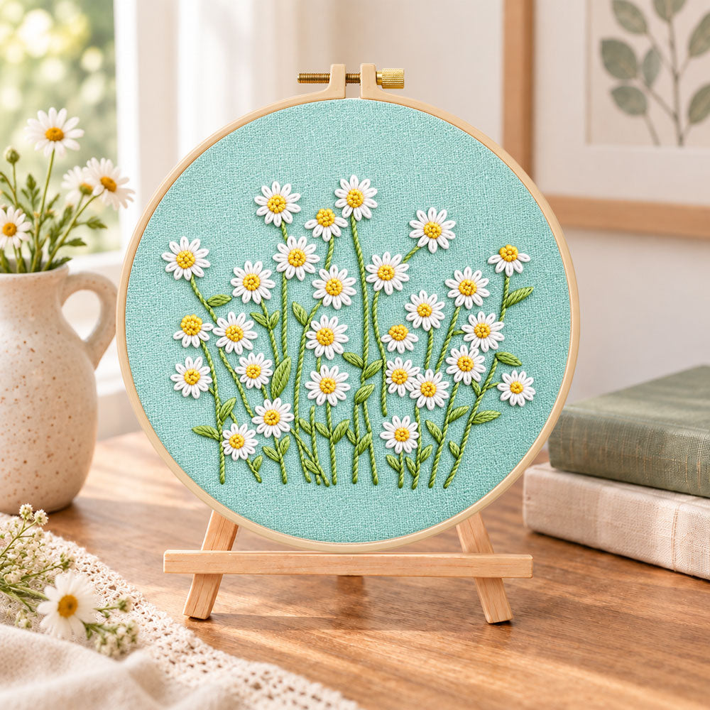 Daisies on teal fabric embroidery kit finished hoop displayed on a wooden stand as cozy tabletop decor