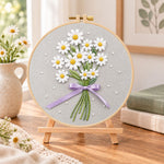 Daisy bouquet with purple ribbon embroidery kit finished hoop displayed on a wooden stand as cozy tabletop decor