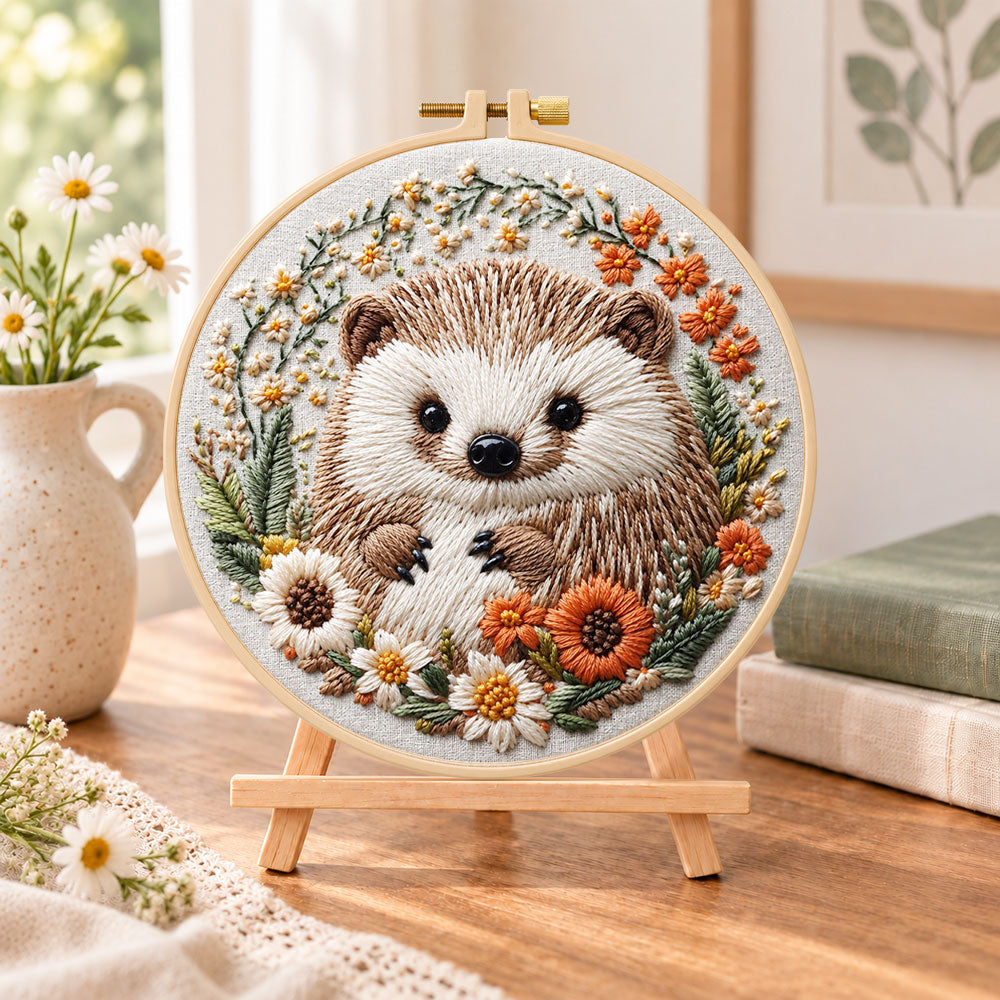 Daisy wreath hedgehog embroidery kit finished hoop displayed on a wooden stand as cozy tabletop decor