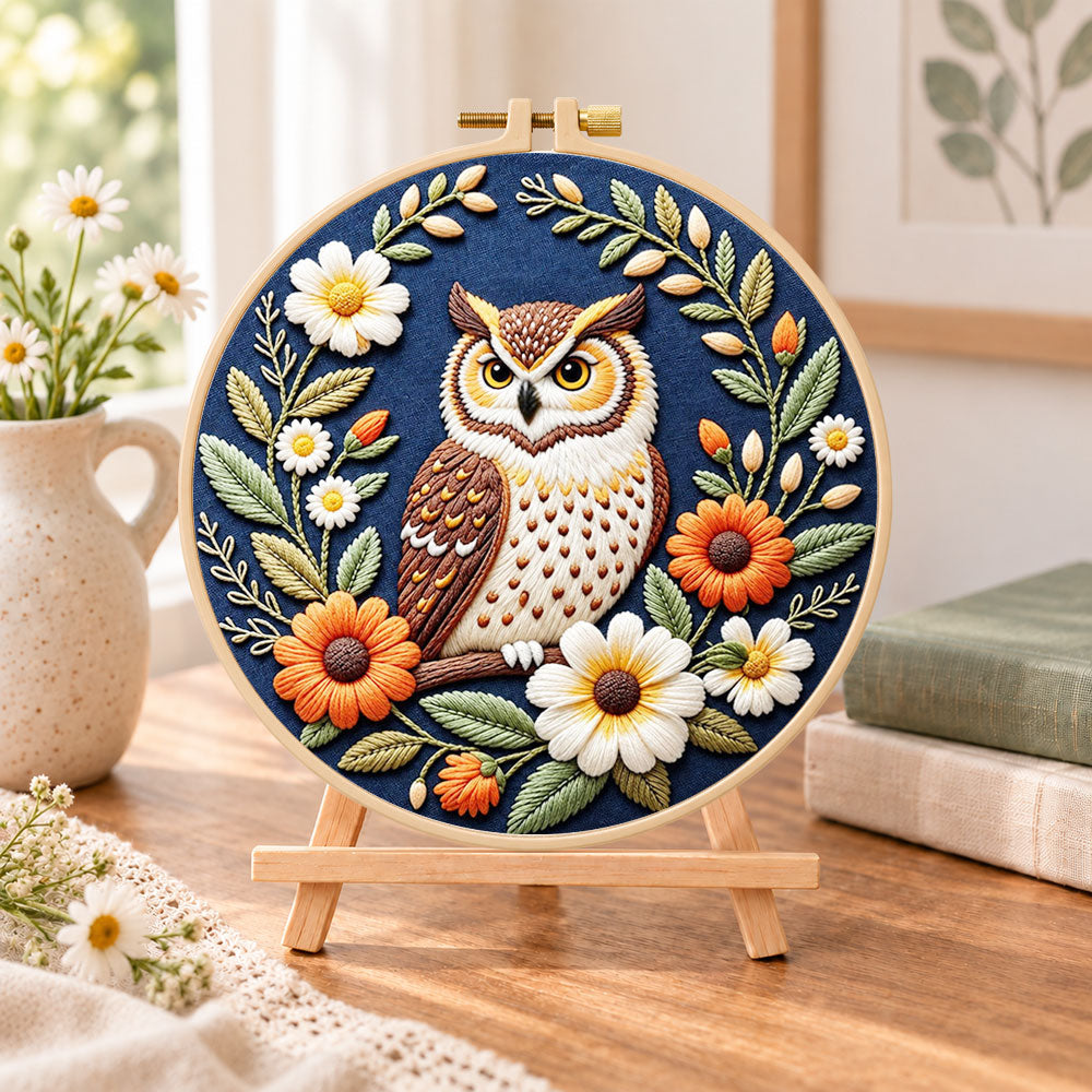 Daisy wreath owl embroidery kit finished hoop displayed on a wooden stand as cozy tabletop decor