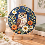 Daisy wreath owl embroidery kit finished hoop displayed on a wooden stand as cozy tabletop decor