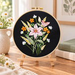 Dark background lilies embroidery kit finished hoop displayed on a wooden stand as cozy tabletop decor
